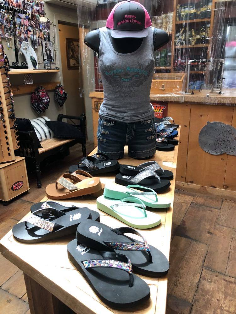 Casual footwear display with various flip-flops and sandals on wooden shelves in a store.